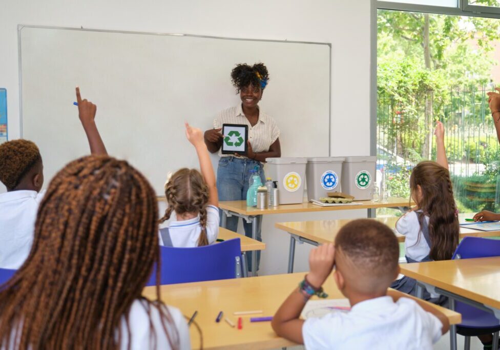 Teacher holding tablet with recycling symbol on screen, teaching environmental awareness to elementary school students